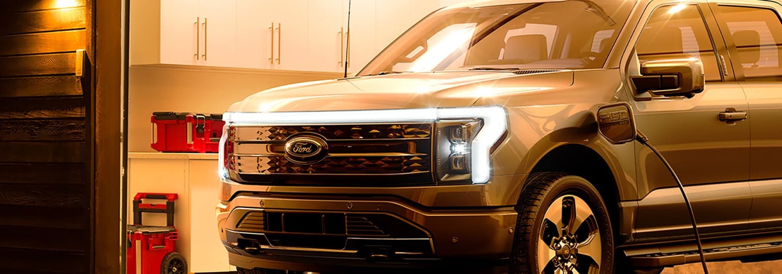 A large, shiny, and metallic pickup truck parked in a garage with headlights on, surrounded by a red toolbox.