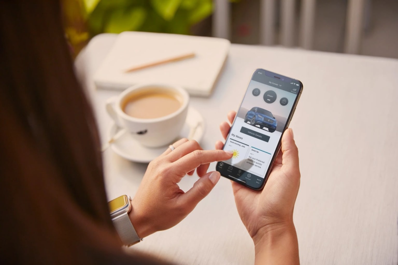 A person browsing a smartphone with coffee and papers on a white table.