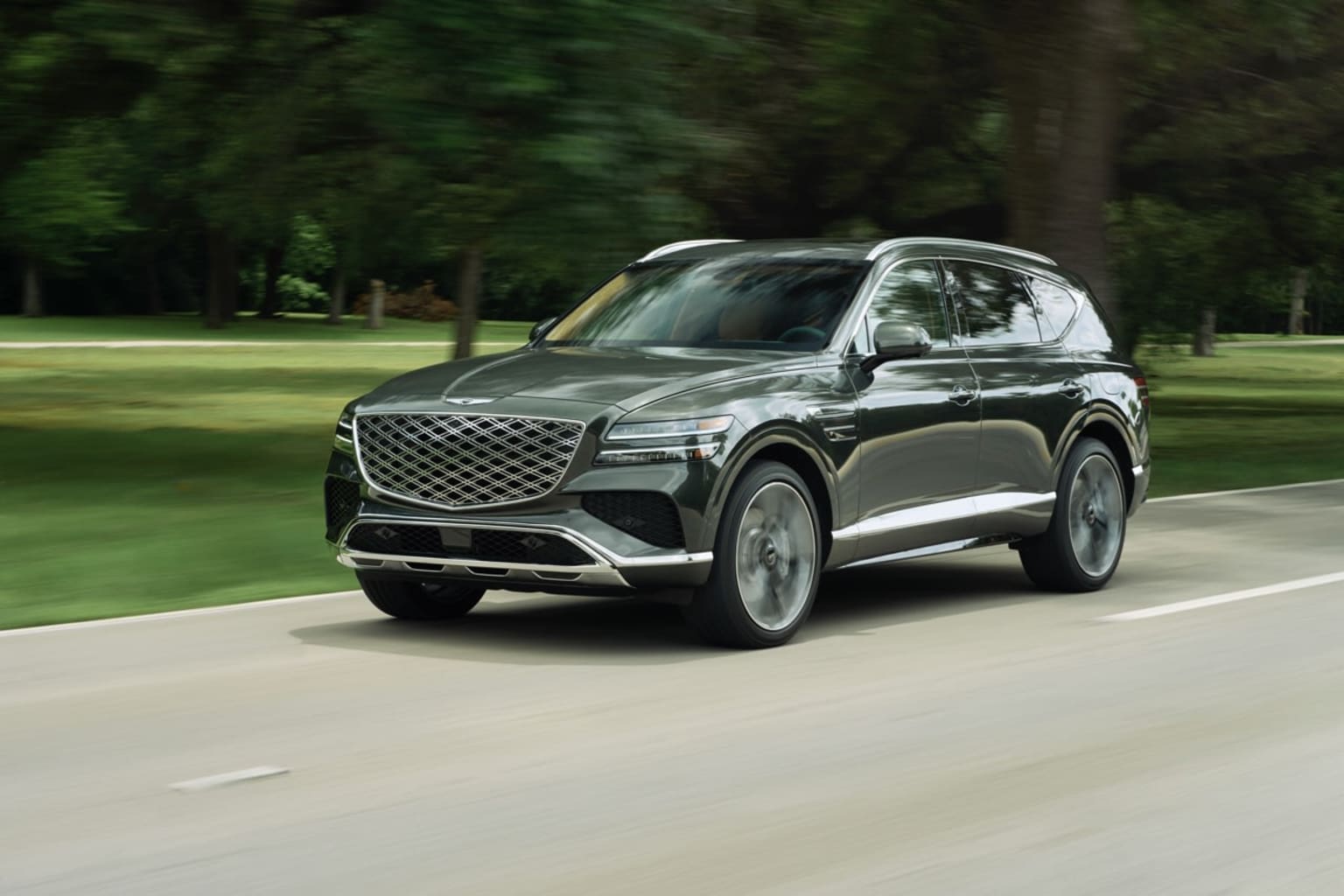 A sleek, black SUV driving down a lush, green road surrounded by trees, creating a blurred background that adds to the sense of motion.