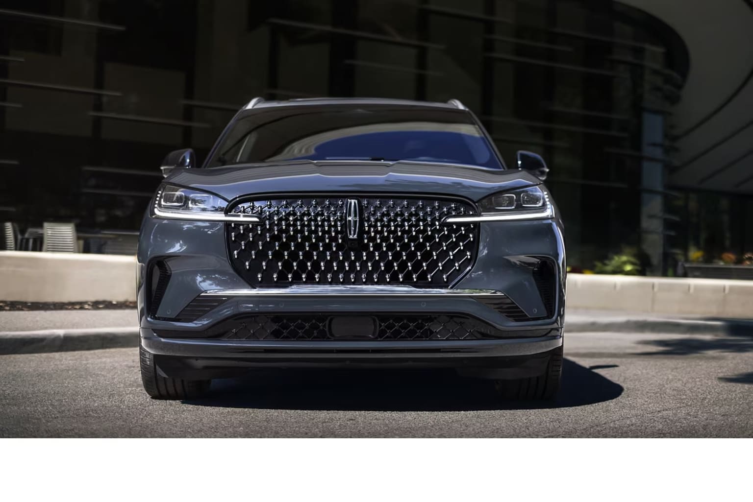 A sleek, gray luxury SUV in front of a modern building with a prominent grille and headlights, casting a bold and imposing presence.