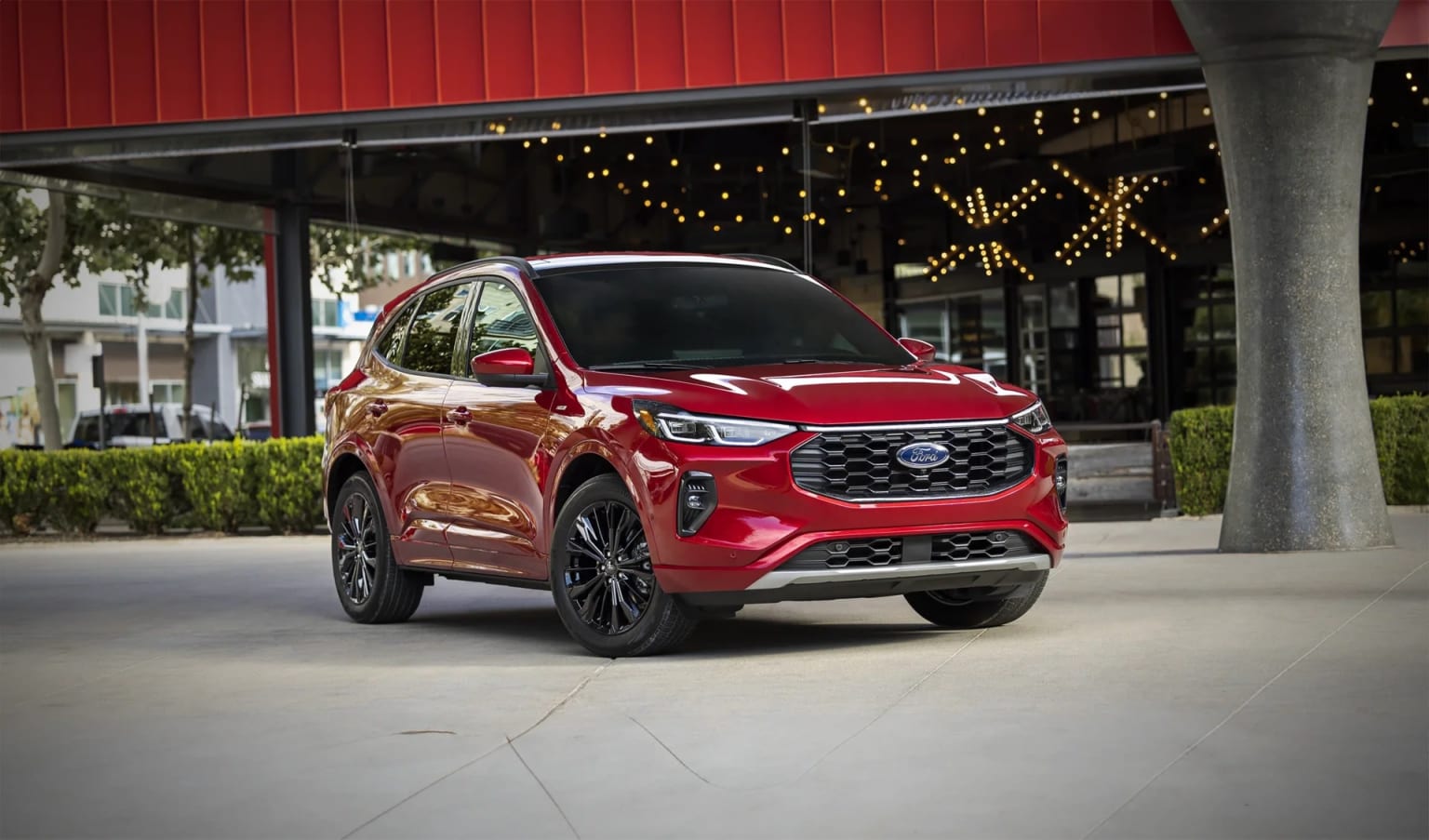 A bright red SUV parked on a concrete sidewalk in front of a building with a red exterior and string lights hanging overhead.