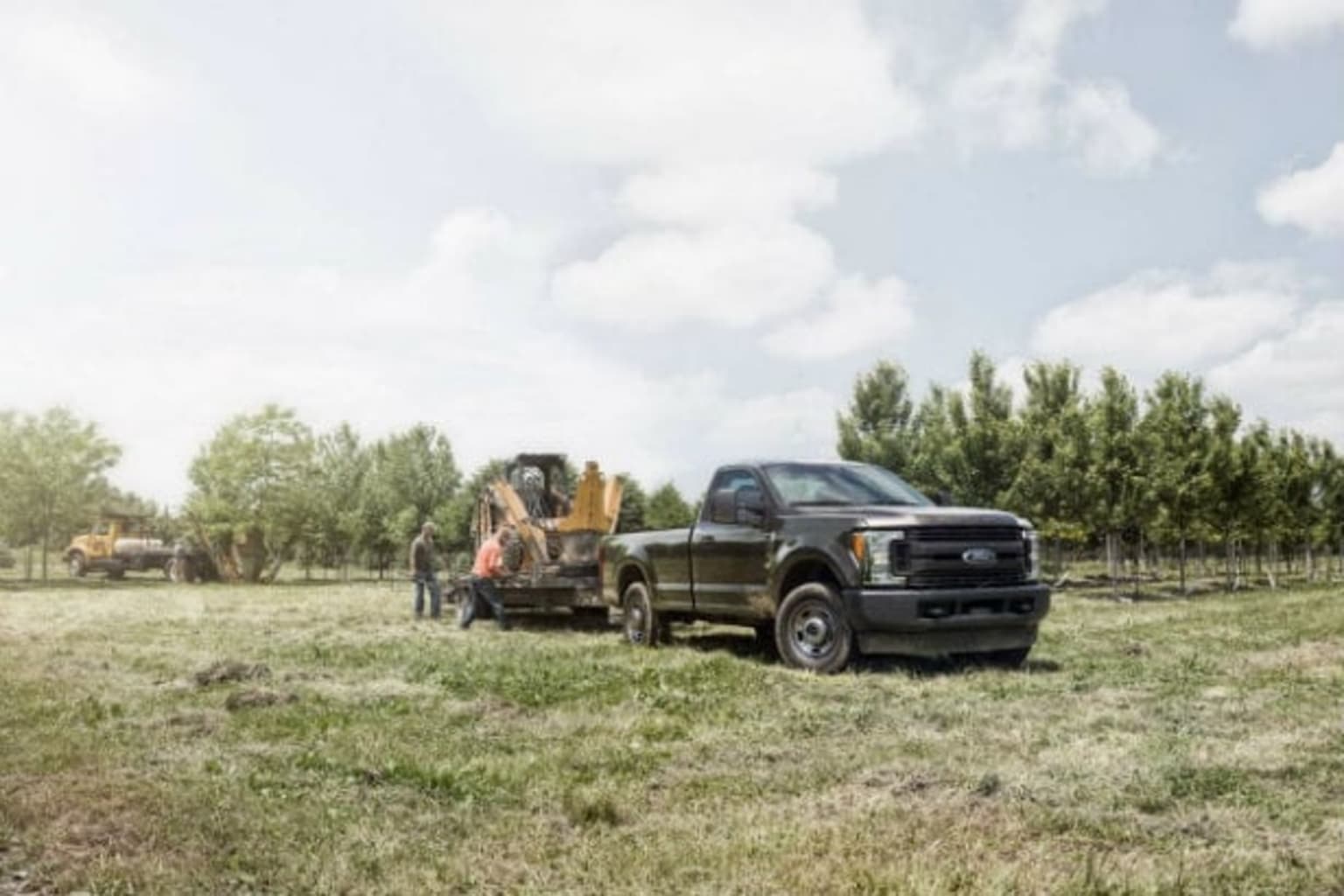 a black truck parked in a field next to a truck with a tractor trailer attached to the back of it
