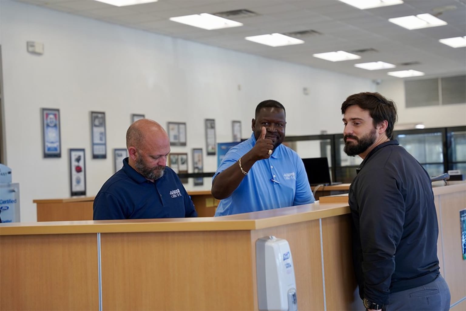 a group of men standing in front of a wooden counter in an office building with water coolers on either side of the counter