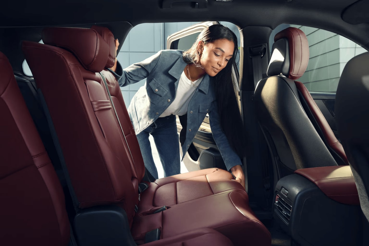 A person in a gray suit is sitting in the backseat of a car, adjusting something in the seat.
