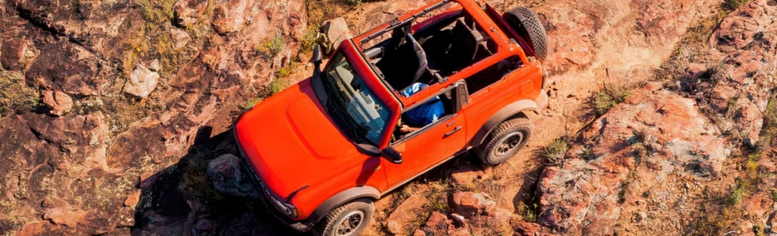 An orange convertible SUV navigates a rocky, arid terrain.