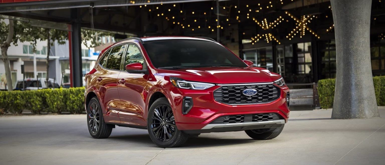 A vibrant red compact SUV on a city street with illuminated buildings and festive string lights in the background.