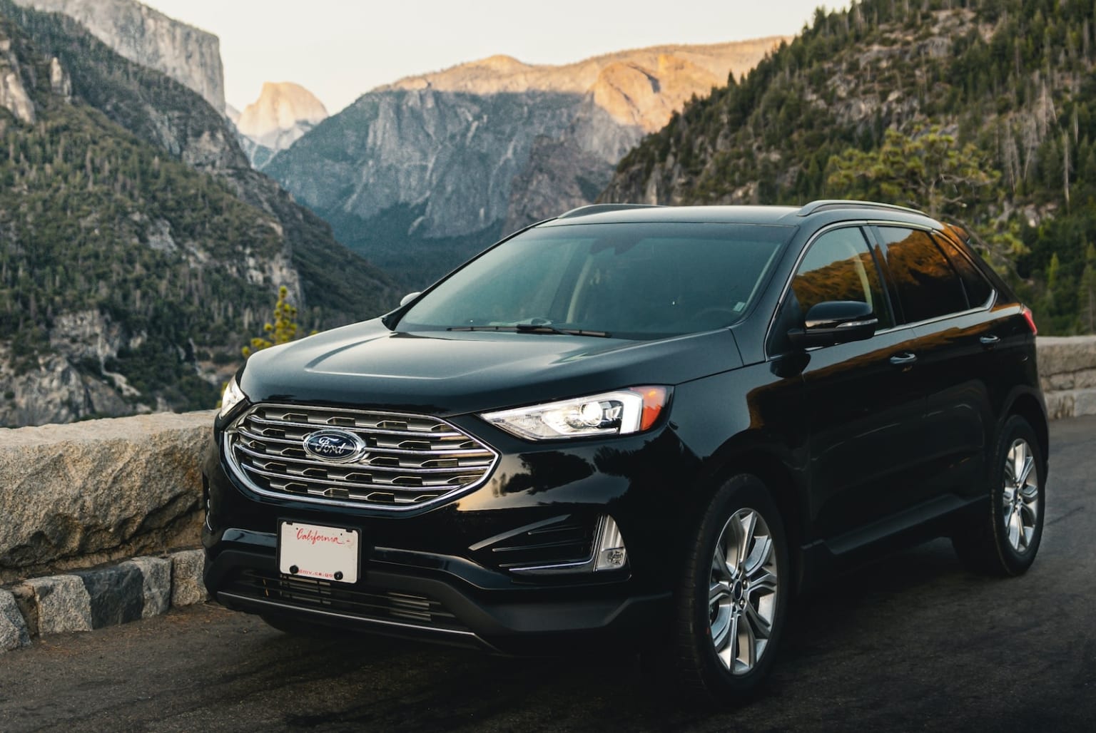 a black suv parked on the side of a road near a mountain with a view of a valley and mountains in the distance