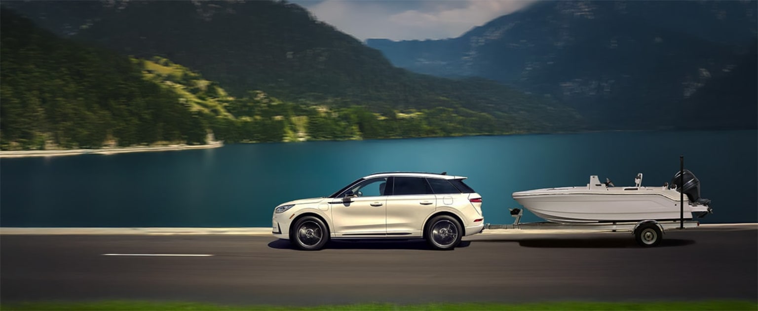 White SUV parked on a road by a serene lake with lush green mountains in the background.