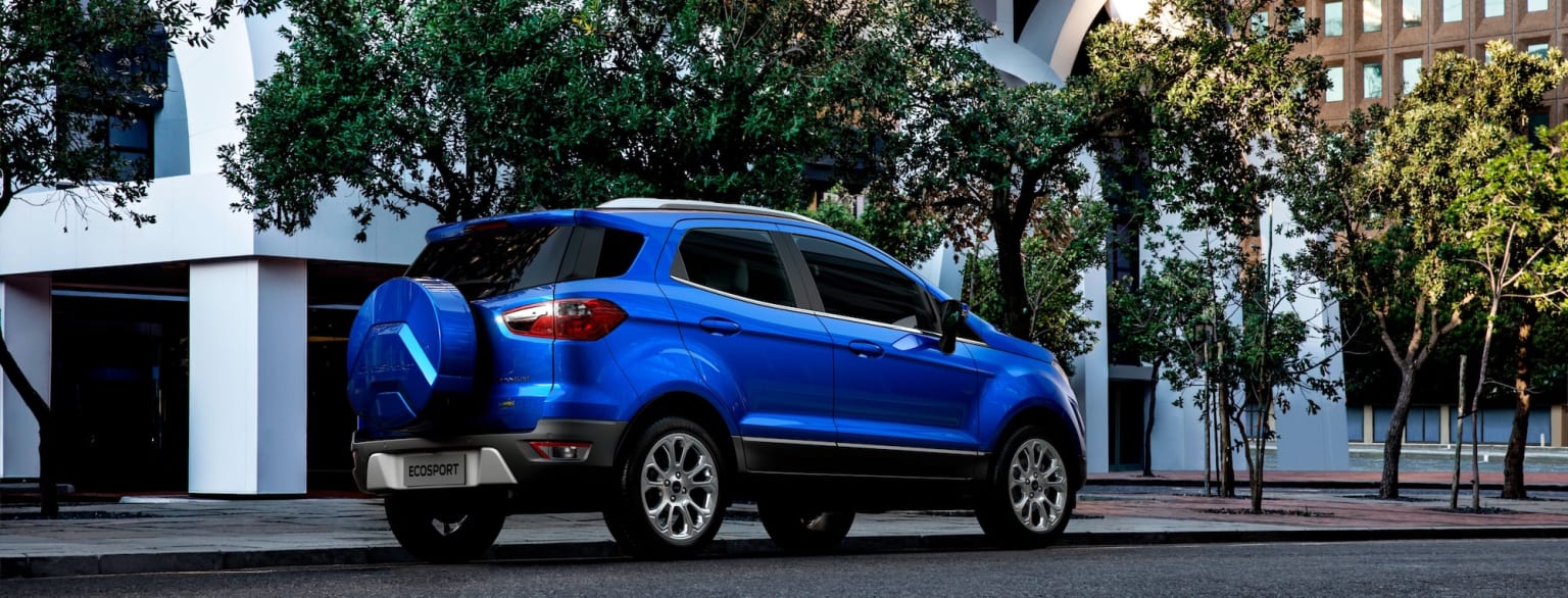 a blue suv parked on the side of a road next to a tree lined street with buildings in the background