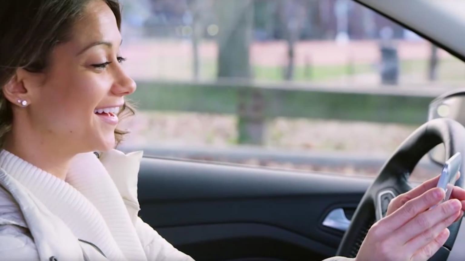 a woman sitting in a car holding a cell phone in her hand and looking at the screen of her car