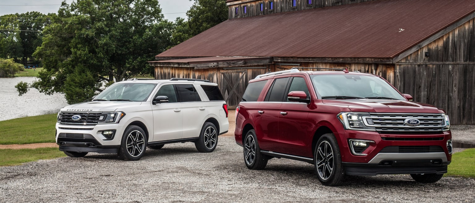 two red and white suvs parked next to each other in front of a wooden building with a barn in the background