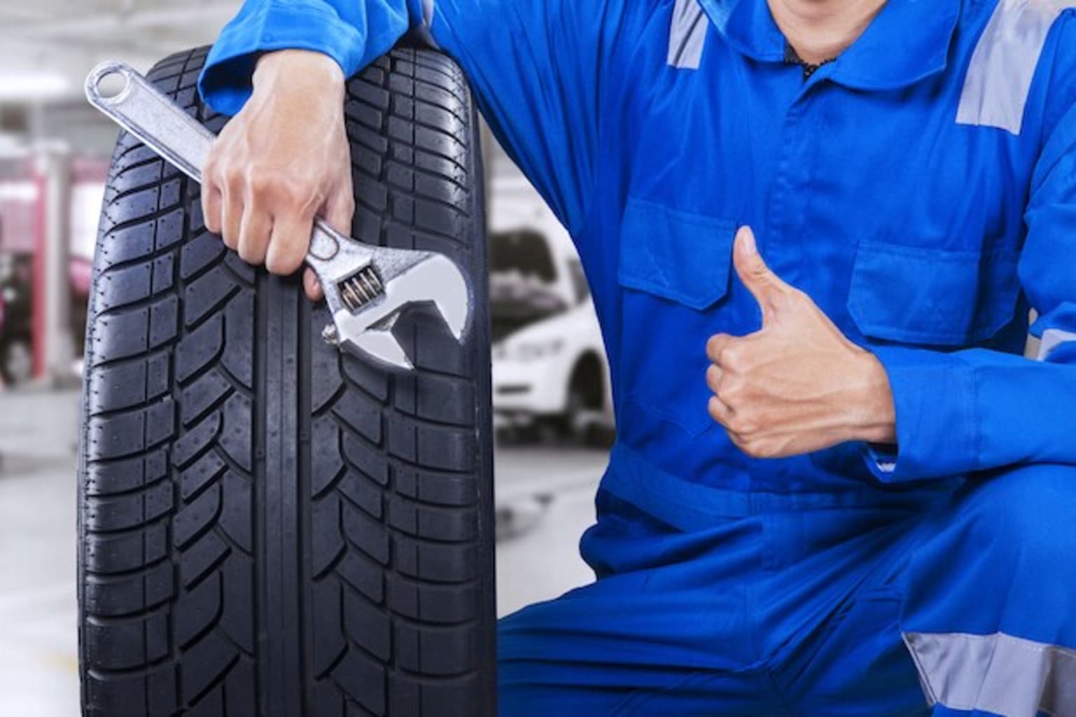 a man in a blue jumpsuit holding a wrench next to a tire with a wrench on it