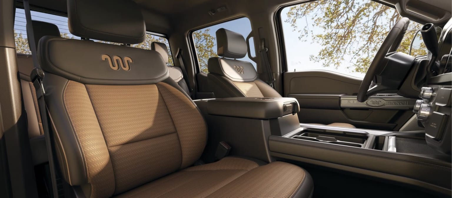 Interior of a vehicle with beige leather seats and a center console in the foreground, with a blurred outdoor scene in the background.
