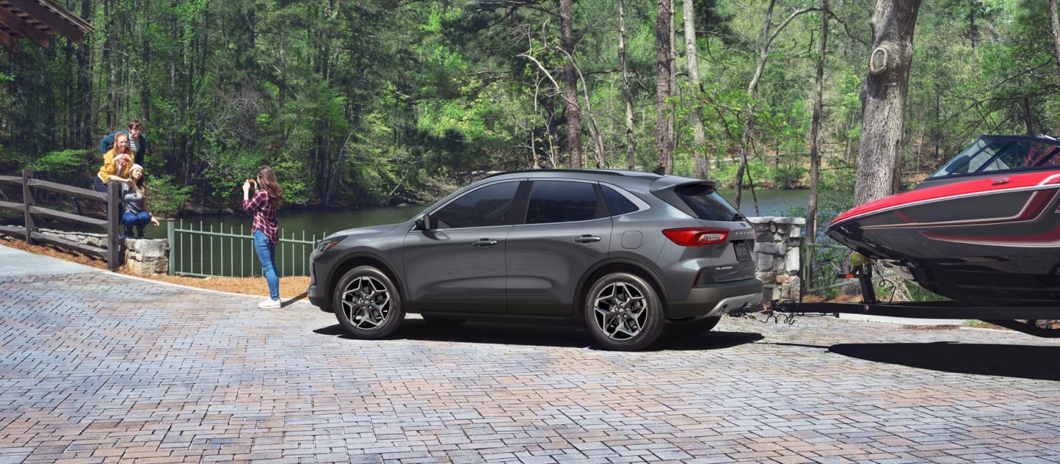 A gray SUV parked on a brick paved driveway surrounded by a lush, forested area with tall trees and greenery.