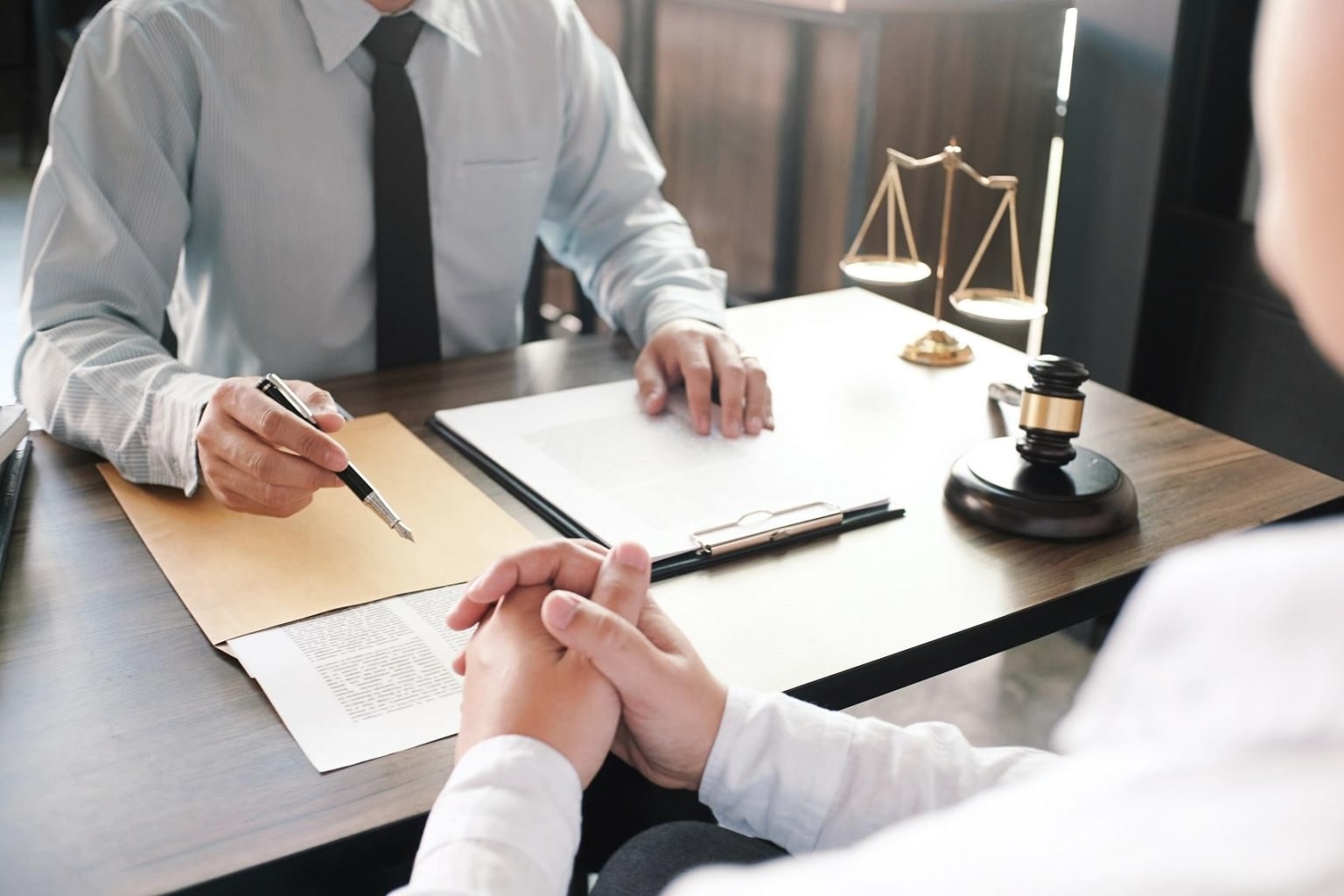 A person in a suit sitting at a desk and signing documents, with a scale of justice and other legal symbols in the background.