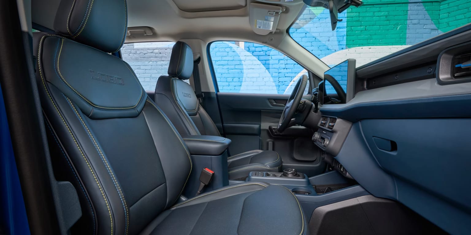 Dark blue leather seats with yellow stitching in foreground, dashboard and colorful brick wall in background.