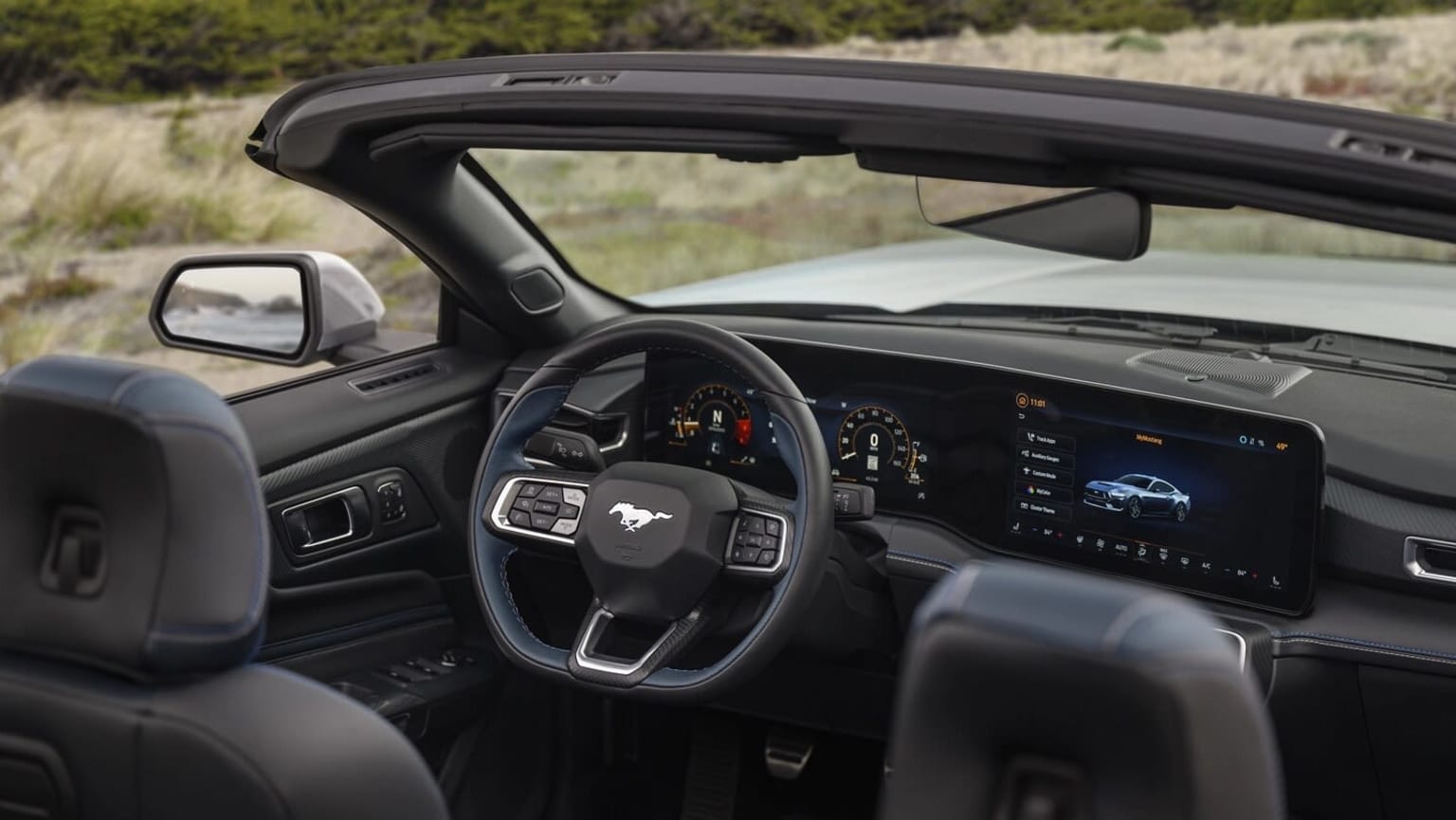 The image shows the interior of a modern vehicle with a sleek dashboard, steering wheel, and a large touchscreen display. The background appears to be a natural landscape, suggesting an outdoor setting.