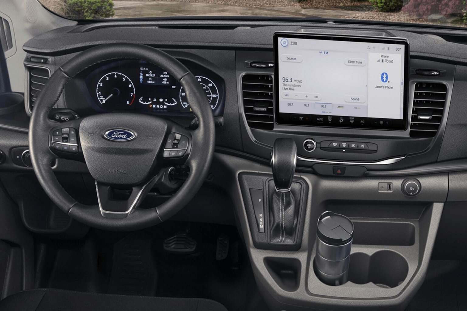 The image shows the interior of a vehicle, with a dashboard featuring a large touchscreen display, a steering wheel, and various controls and buttons. The background appears to be a road or outdoor environment, suggesting the vehicle is in motion.