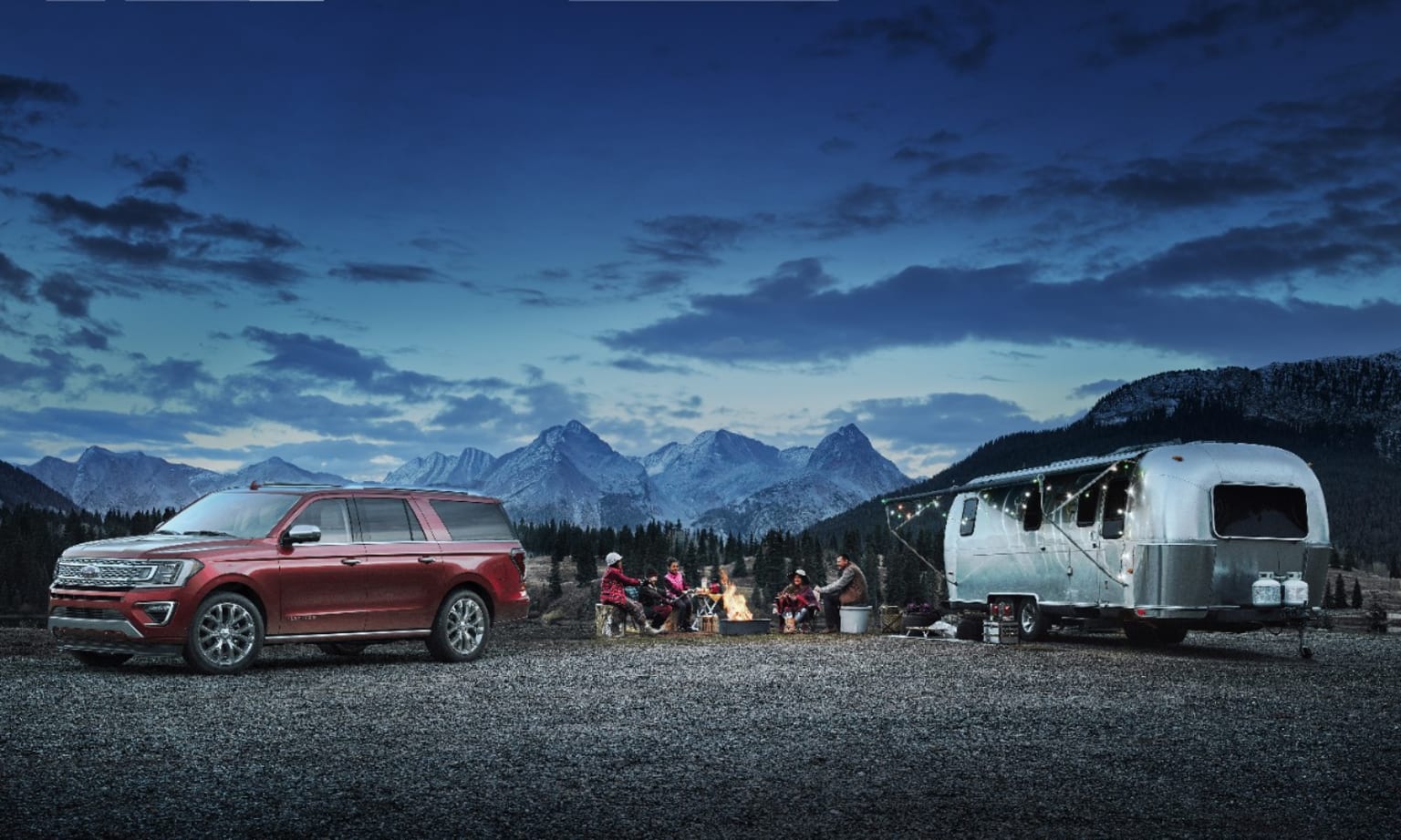 a red truck parked next to a camper in front of a mountain range at night with people standing around