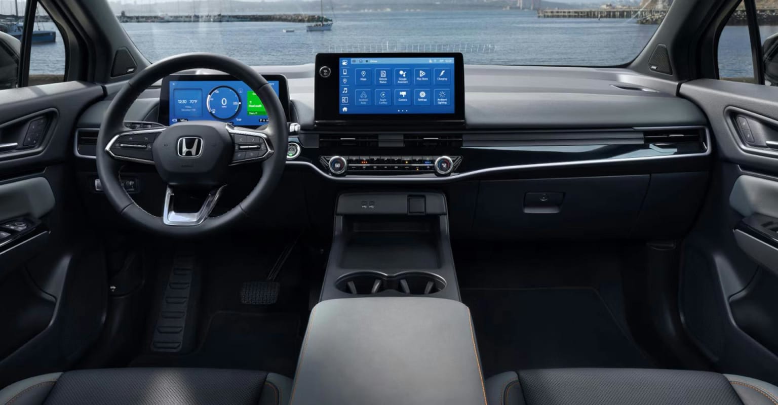 A modern car dashboard with a large touchscreen and digital display in the foreground, with a blurred waterfront scene in the background featuring boats and buildings.
