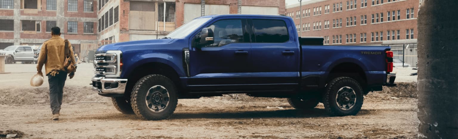 A man walking away from a blue pickup truck in a dirt lot in front of a brick building.