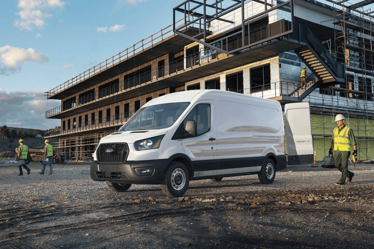 A white delivery van parked in the foreground of a construction site, with a partially completed multi-story building visible in the background and several construction workers in the vicinity.