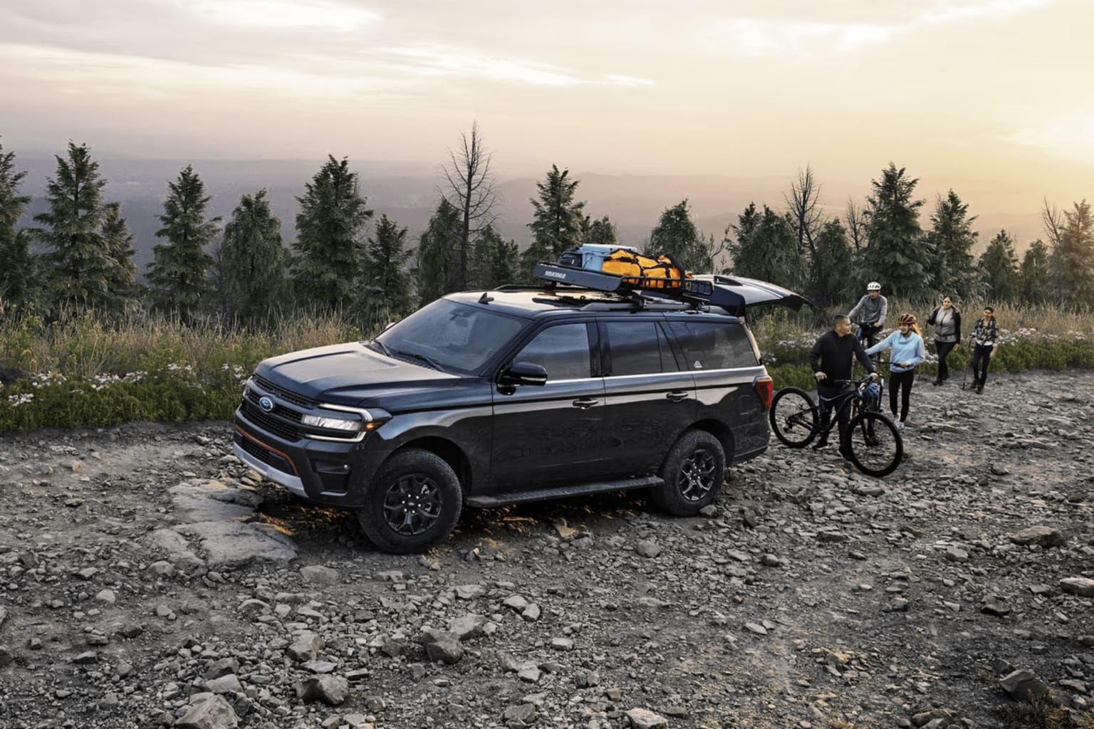 Off-road vehicle with outdoor gear on roof in forest setting with people on bicycles.