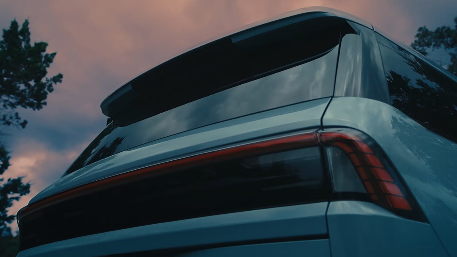 Sleek, modern SUV with a distinctive rear design against a backdrop of trees and a dramatic sky.