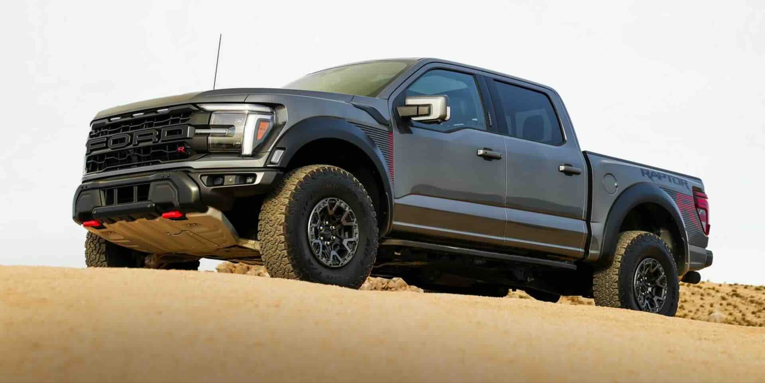 An image of a gray truck parked on a sandy dune with a clear sky in the background.