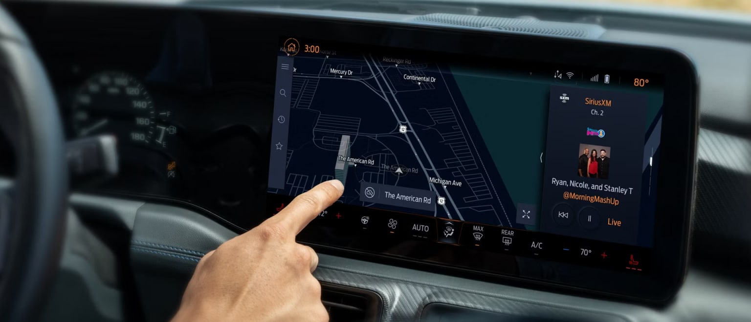 A hand is touching a touchscreen display in a vehicle, showing a map and various information on the dashboard.