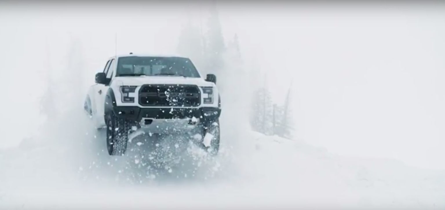 a white truck driving through a snow covered forest in the wintertime with snow falling on the ground and trees in the background