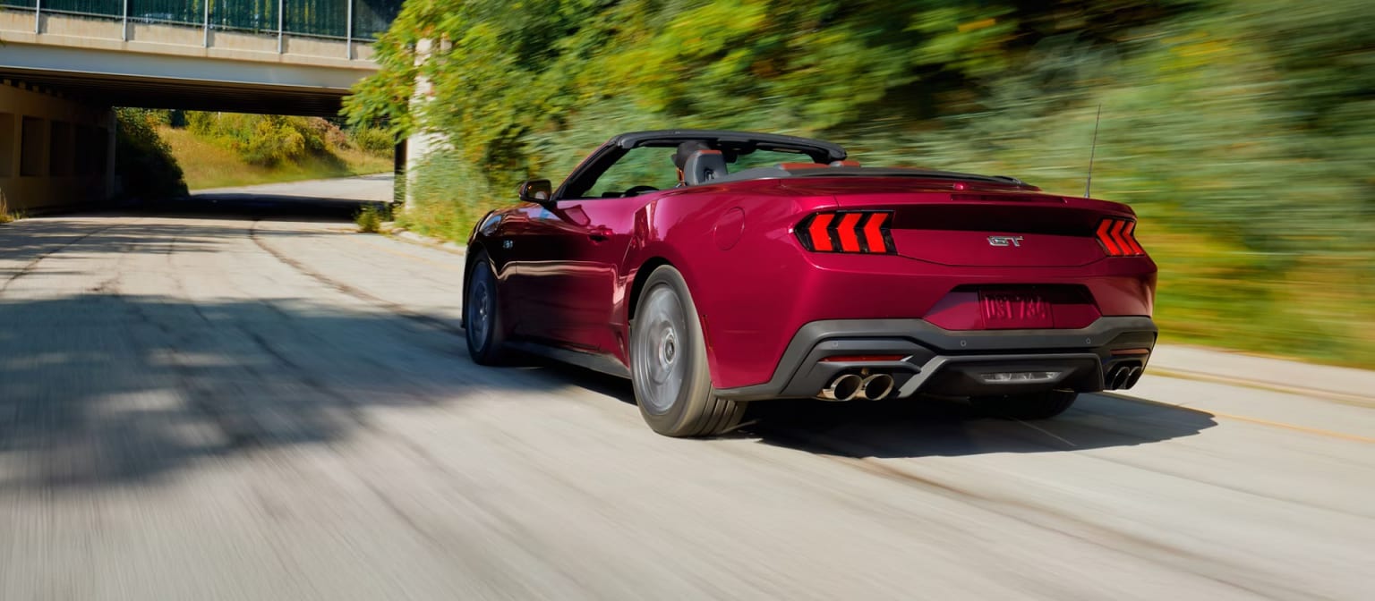 A bright red sports car speeding down a road surrounded by lush greenery with a bridge in the background.