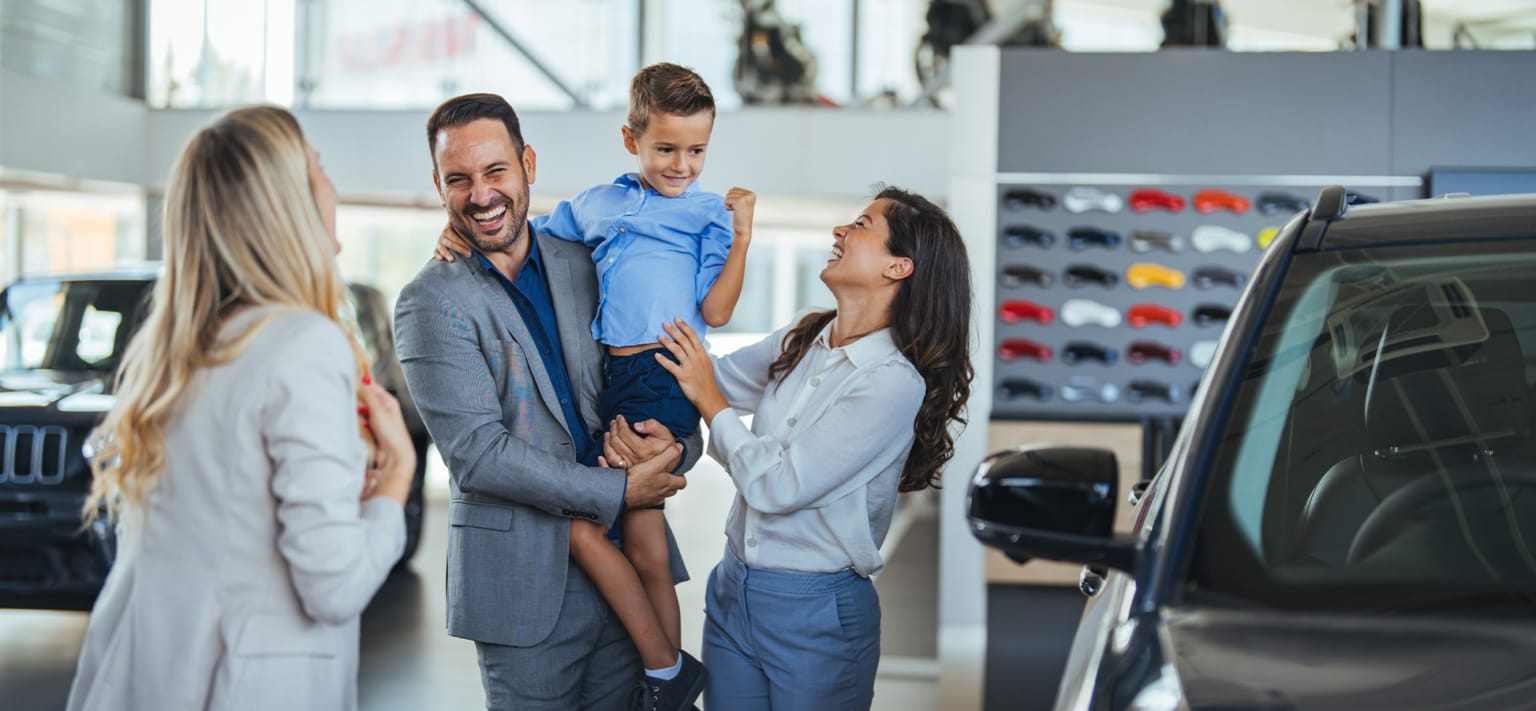 A happy family looking at a new car in a brightly lit showroom with rows of car models in the background.