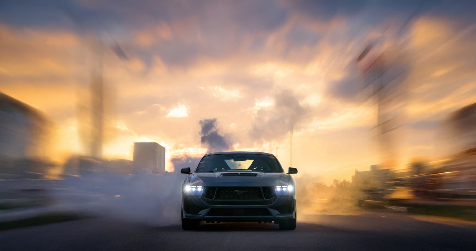 Blurred SUV driving on a road with colorful sky and dramatic clouds in the background.