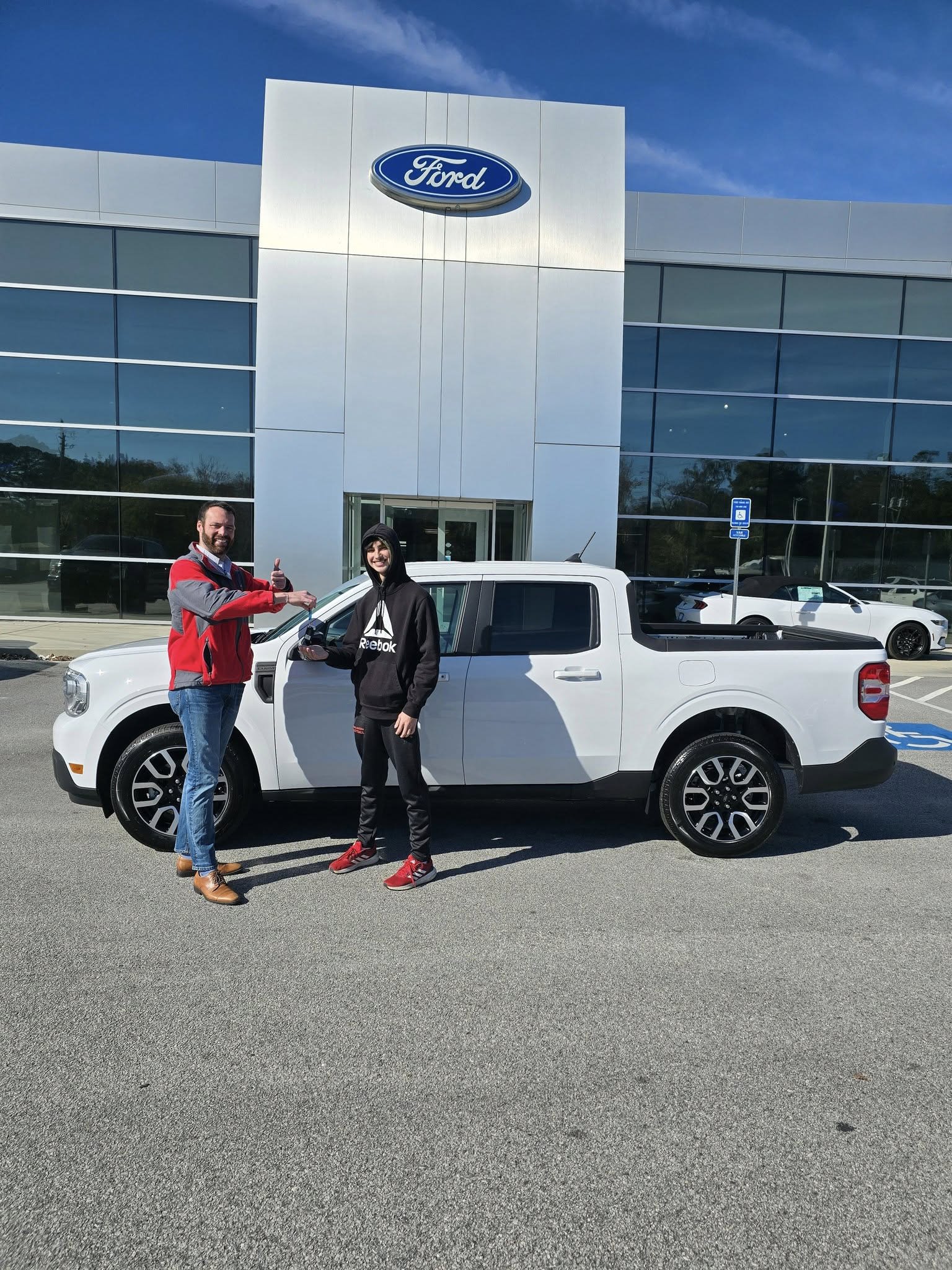The image shows a white pickup truck parked in front of a dealership building with the logo prominently displayed.