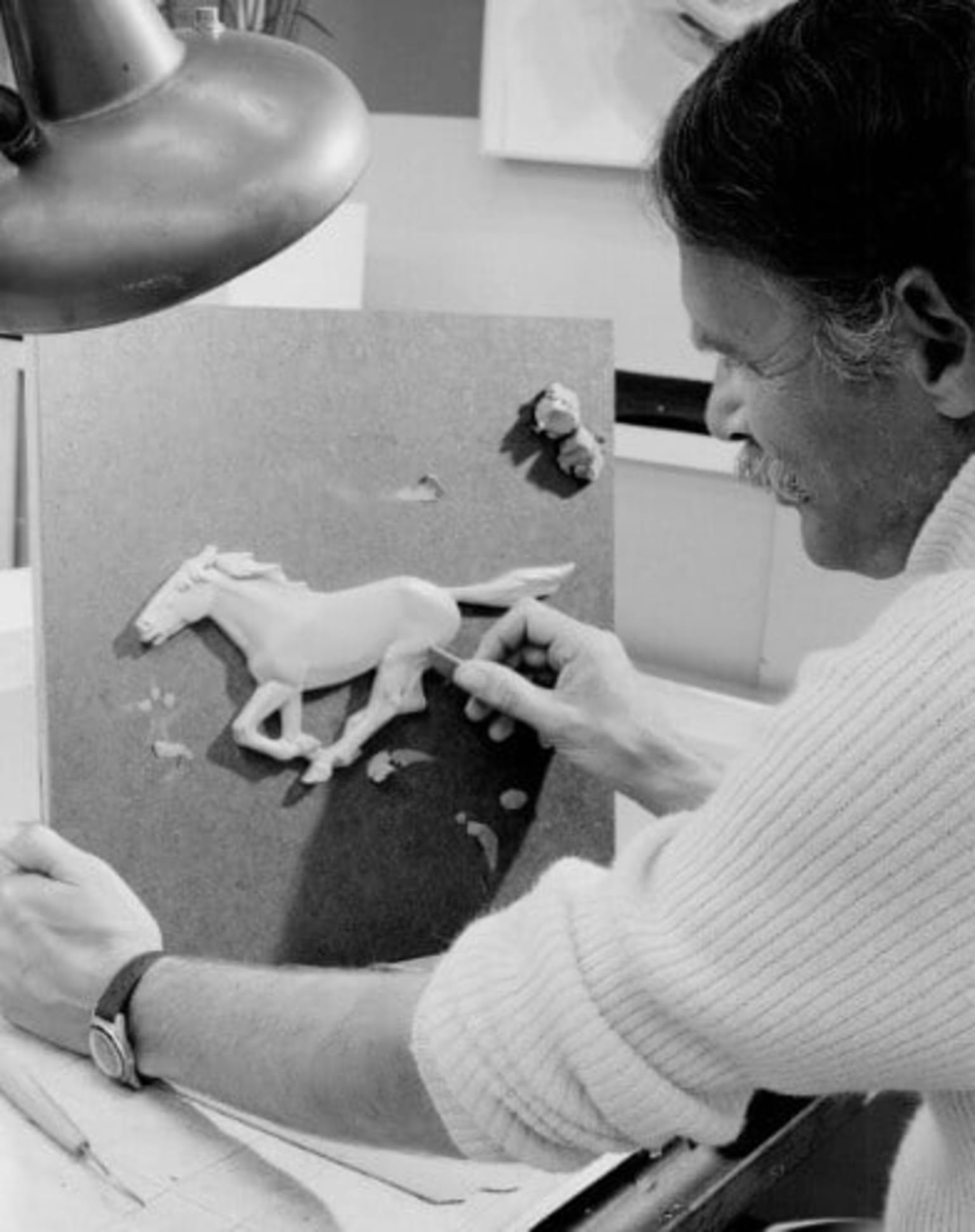 a woman sitting at a desk working on a piece of paper with a horse sculpture on top of it