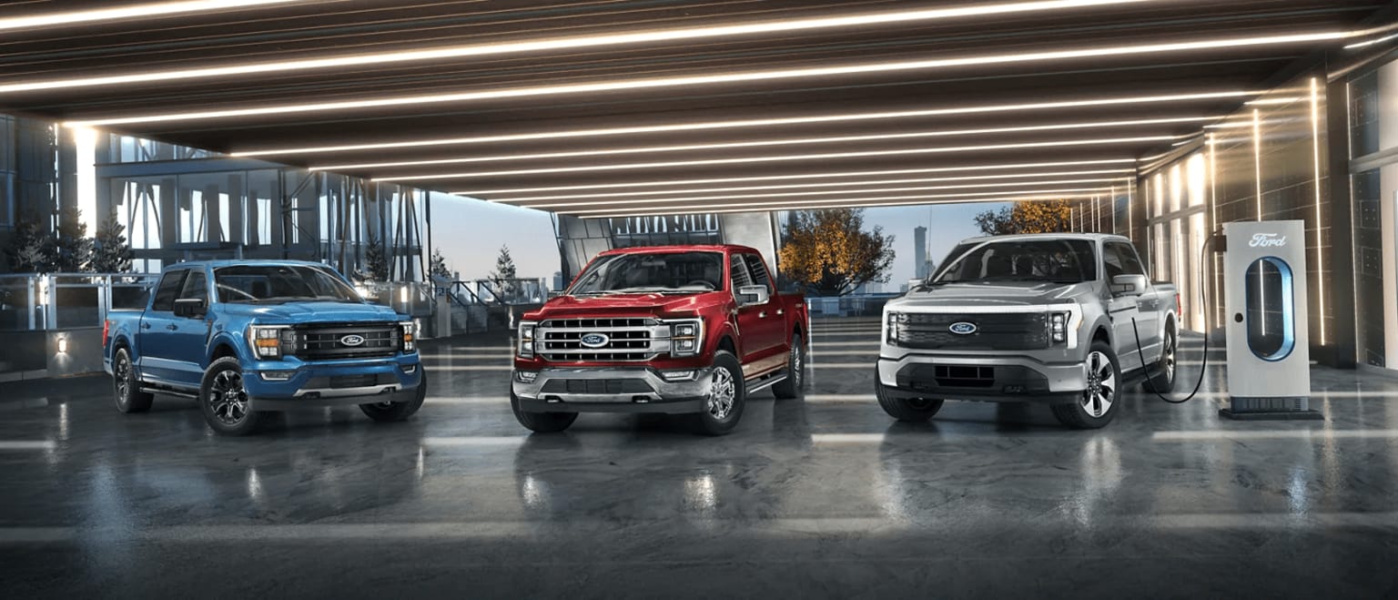 a group of four pickup trucks parked next to each other in front of a building with a sky background