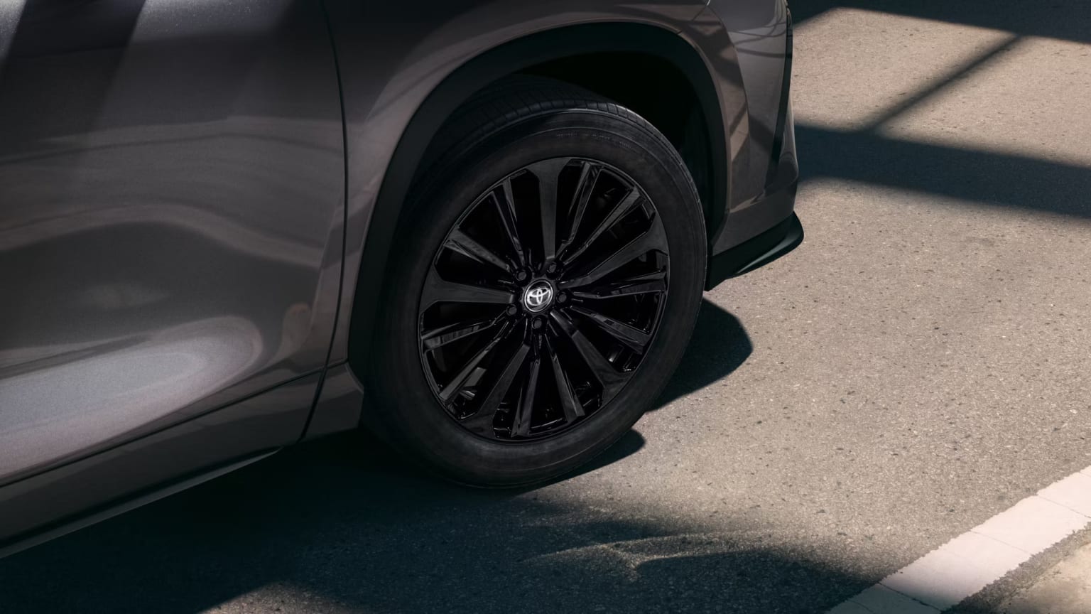 Close-up view of a black alloy wheel on a vehicle with shadows from the surroundings.