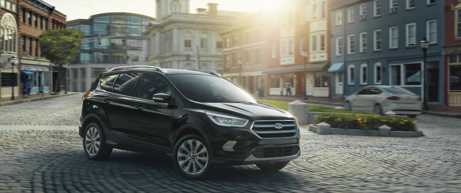 a black suv is parked on a cobblestone street in a city at sunset or sunrise, with the sun shining on the buildings