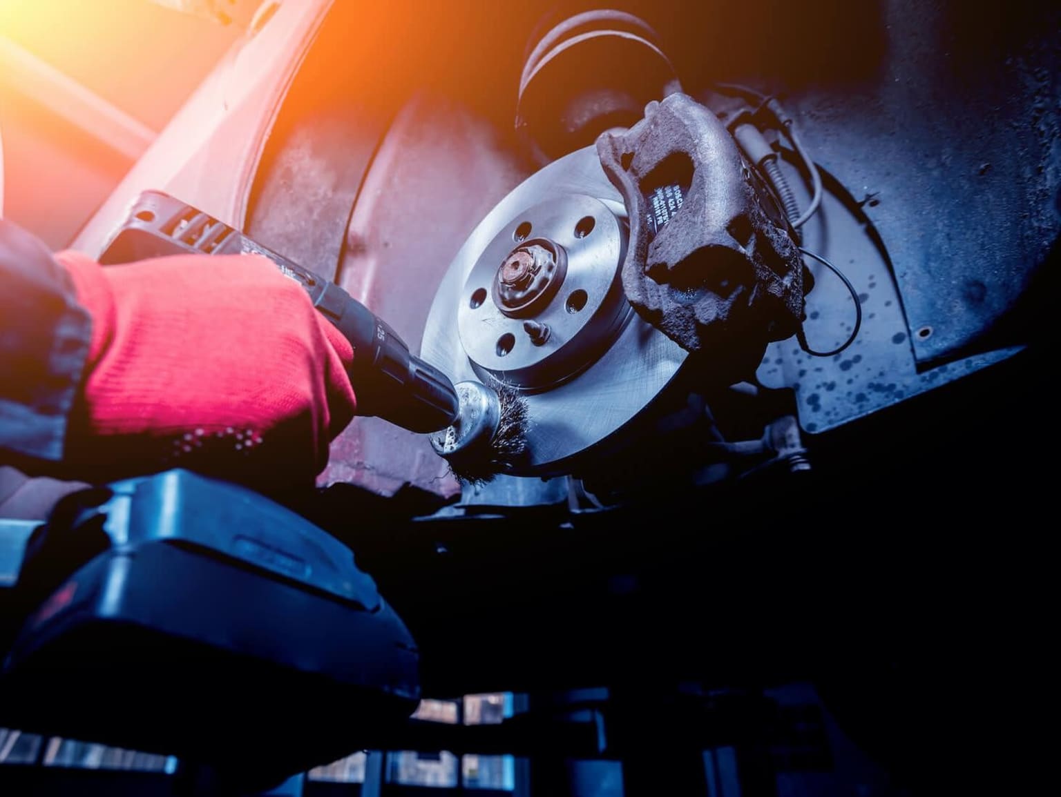 A close-up view of a mechanic's hands working on the brakes of a vehicle, with the engine and other components visible in the background.