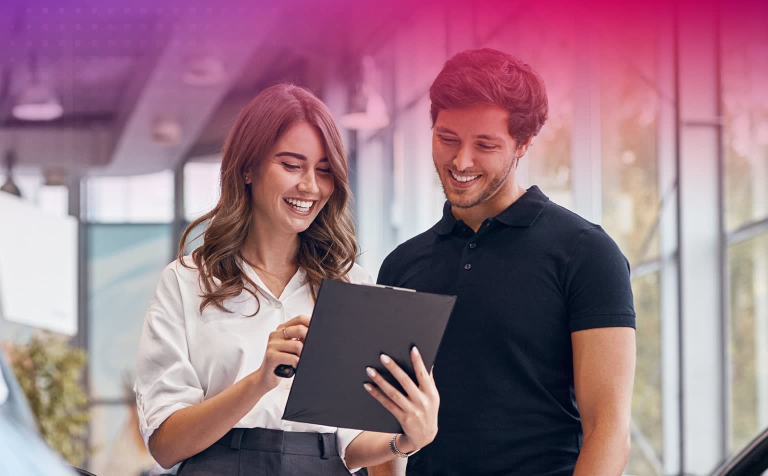 A smiling young couple looking at a tablet together in a modern office or workspace setting.