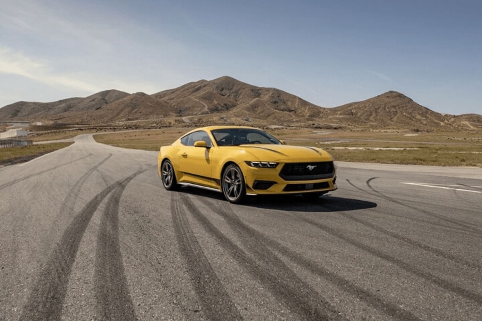 A yellow sports car driving on a road in a desert landscape with mountains in the background.