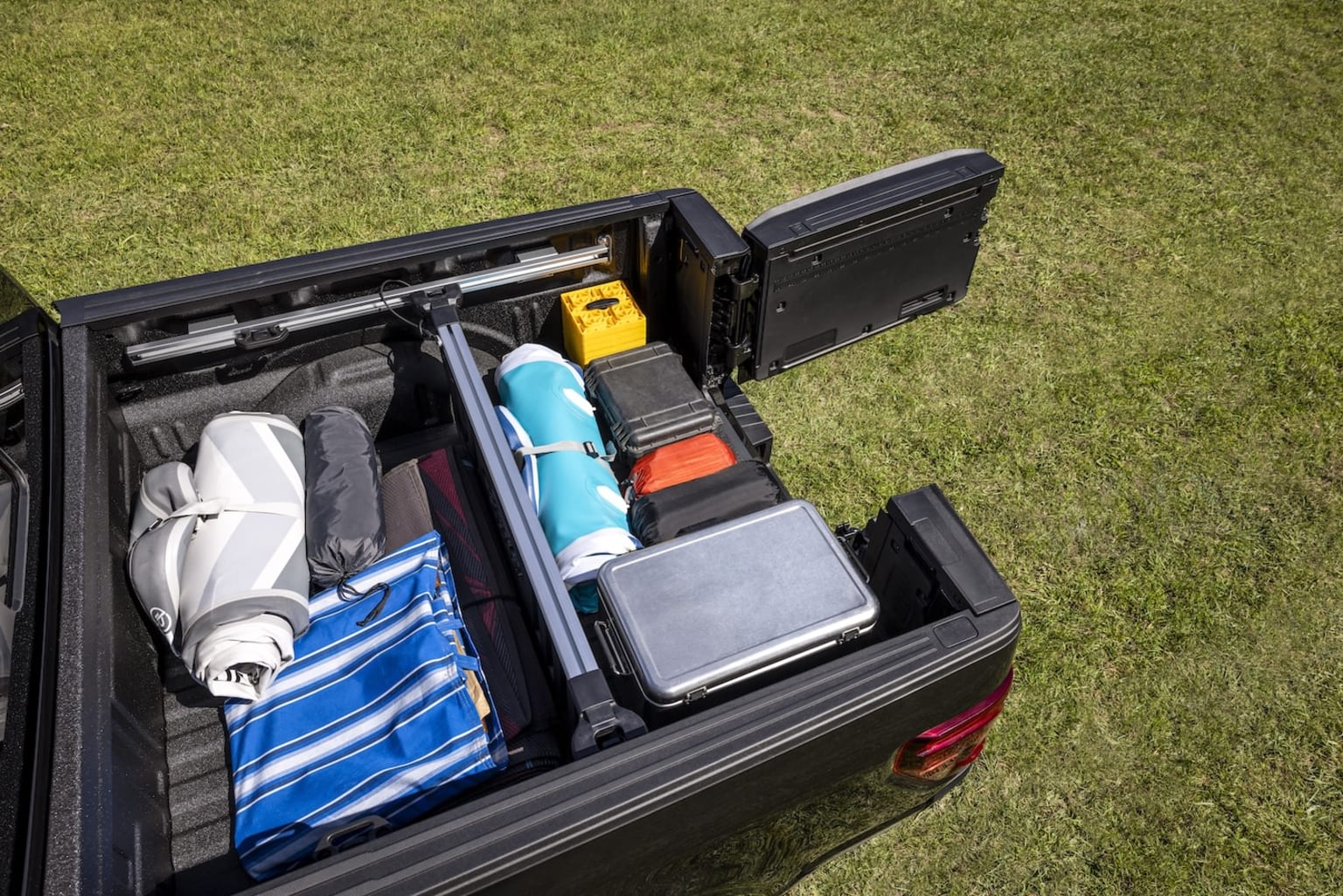 An open car trunk filled with various items, including clothing, bags, and other personal belongings, set against a grassy background.