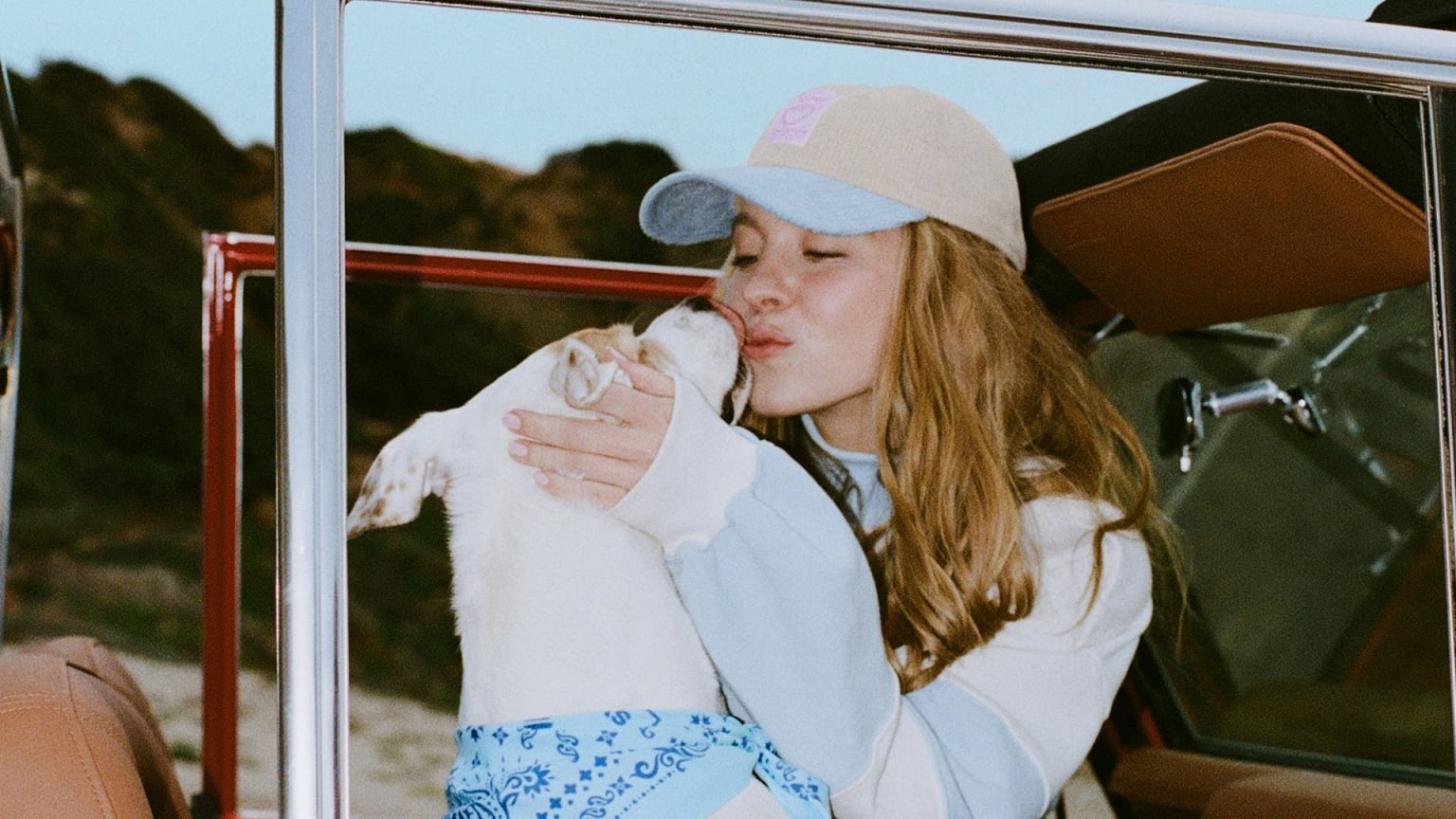 a woman is holding a dog in her lap while sitting in a car with a hat on her head