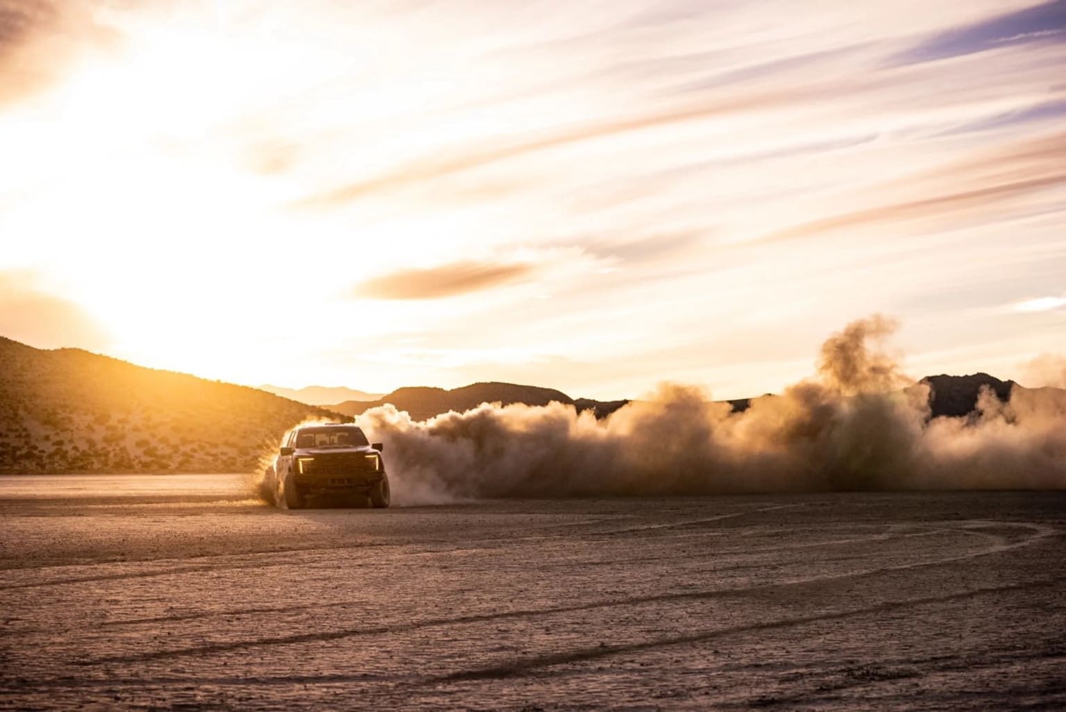Ford Raptor R driving through dusty terrain with mountains in the background during sunset.