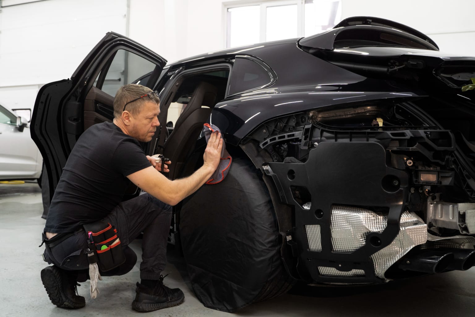 A technician in a black uniform is detailing the interior of a large, dark-colored vehicle in a well-lit garage setting.