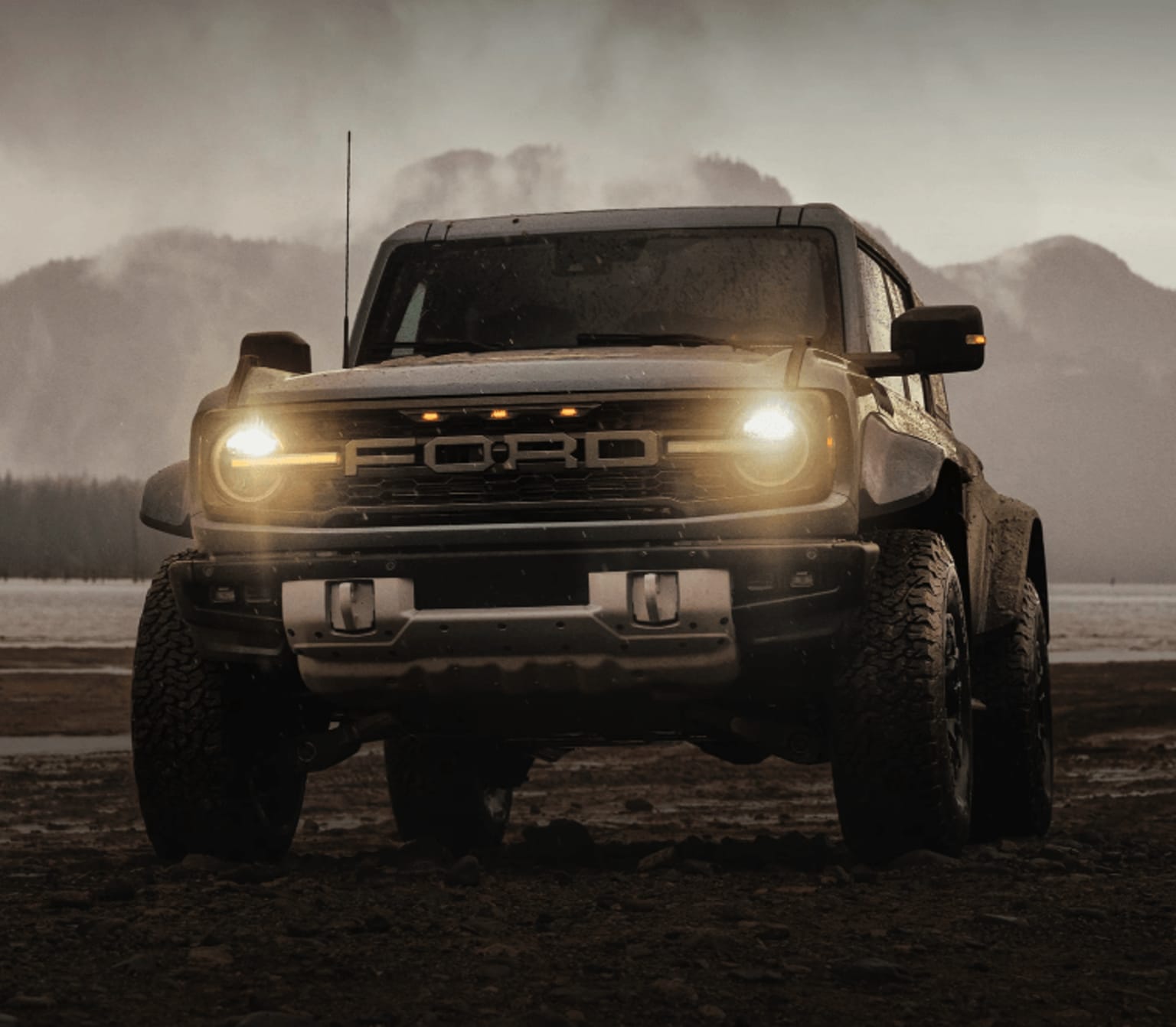 An image showing a lifted SUV with headlights on, set in a snowy mountainous landscape.