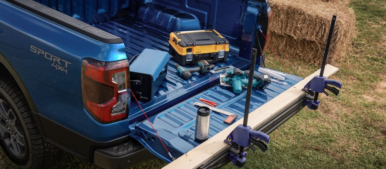 Image of a blue pickup truck filled with various tools and equipment against a backdrop of a grassy field