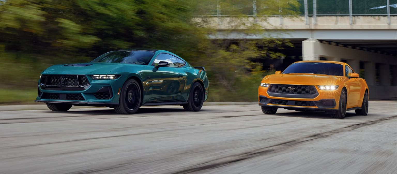 Two high-performance SUVs in vibrant teal and bold orange colors are speeding down a road with blurred surroundings, suggesting a dynamic and energetic scene.
