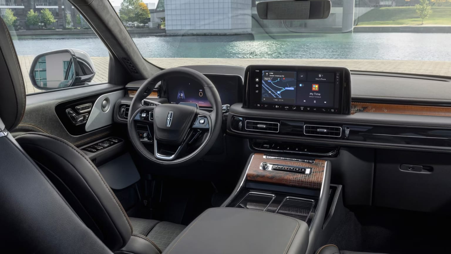 The image shows the interior of a modern vehicle, with a sleek dashboard, a large touchscreen display, and a steering wheel. The background outside the vehicle appears to be a cityscape with glass buildings.
